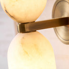 Close-up of the metal collar joining the two lit shades of the Nexus Modern Alabaster Wall Light.