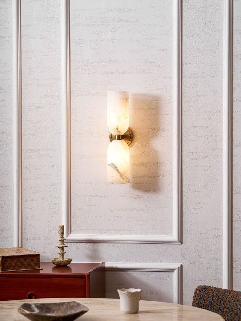 The Nexus Modern Alabaster Wall Light lit on a panelled dining room wall above a wooden sideboard.