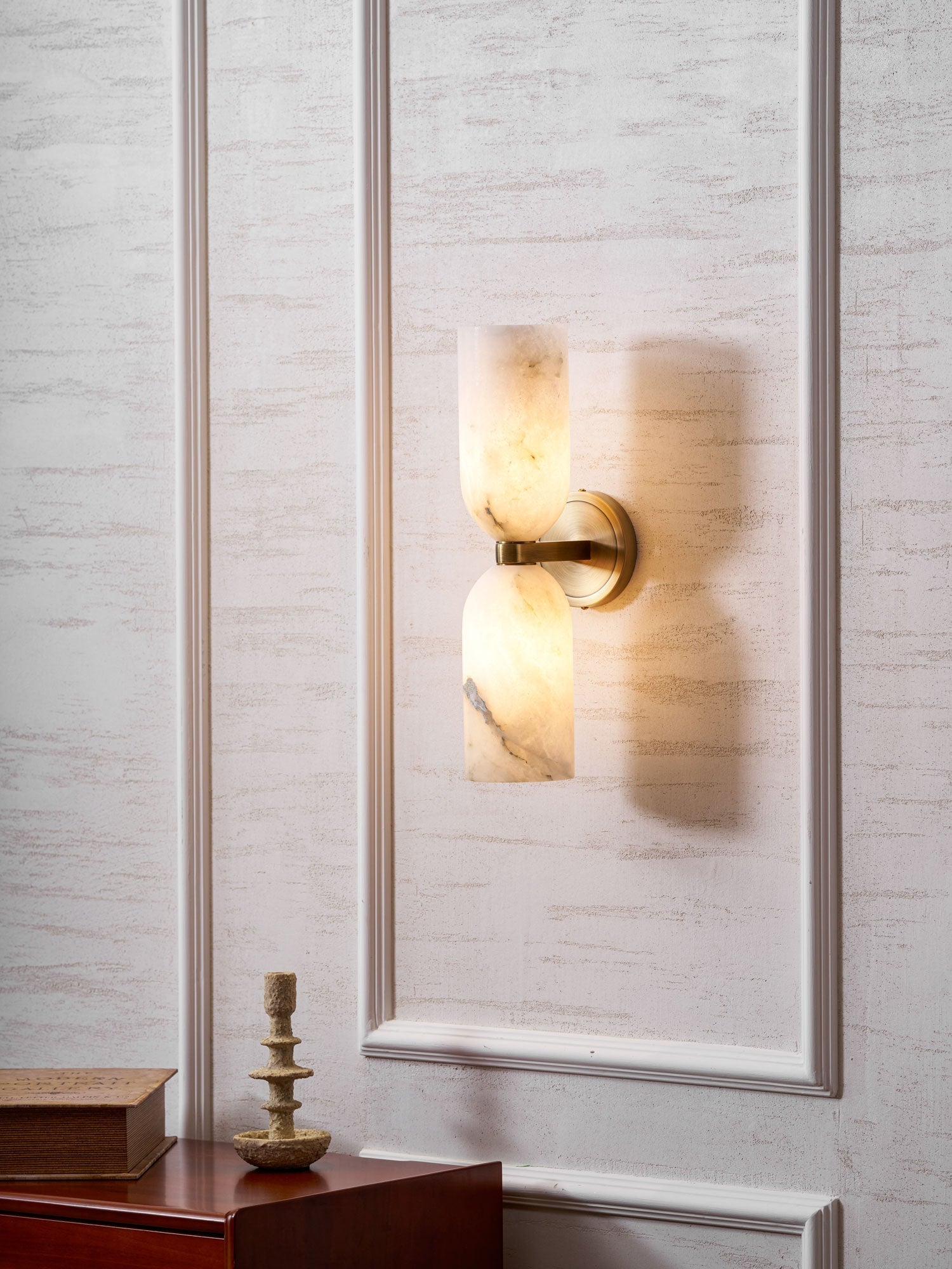 Angled view of the lit Nexus Modern Alabaster Wall Light, its warm glow washing the panelled wall behind.