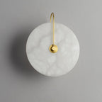 Unlit gold-arm Elaris wall light on grey, the pebbled translucency of the alabaster clearly visible.