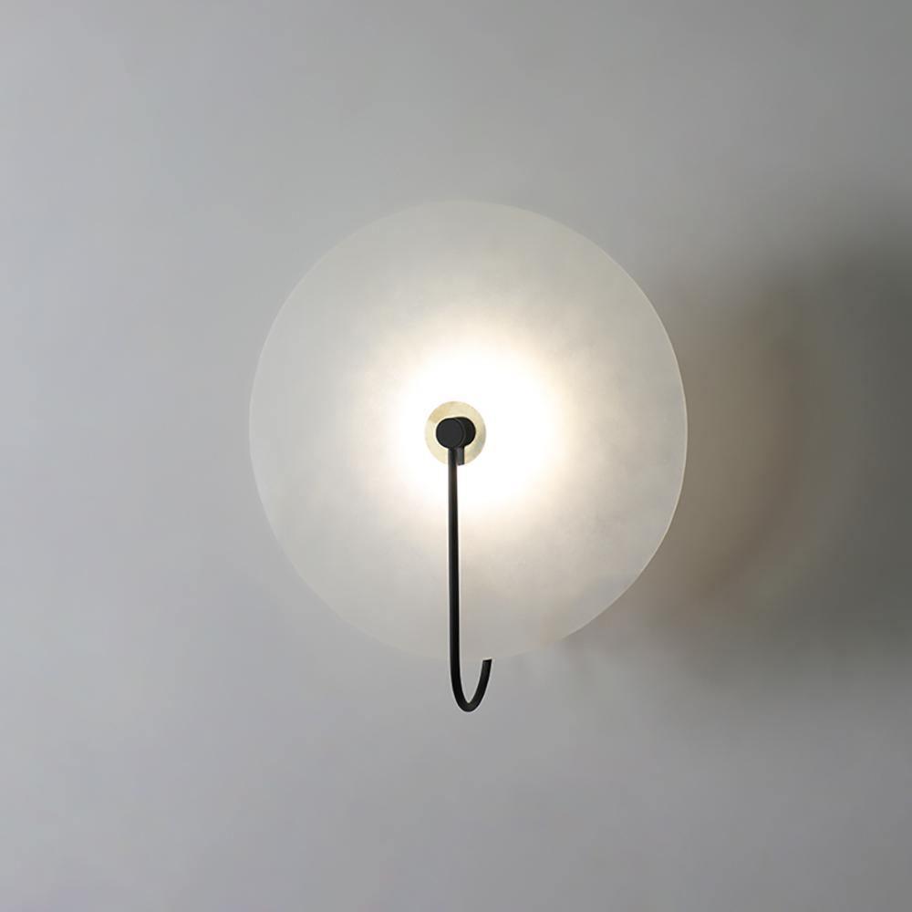Black-arm Elaris wall light lit on grey, the brass collar at the centre catching the light.