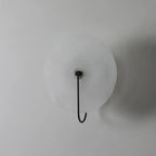 Unlit black Elaris wall light on a white wall, the hook arm curving down past the disc edge.
