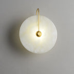 Elaris alabaster wall light with a gold arch arm, lit and glowing warm against a soft grey wall.
