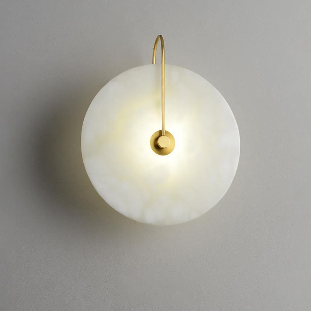 Elaris alabaster wall light with a gold arch arm, lit and glowing warm against a soft grey wall.