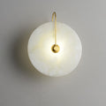 Front view of the gold-arm Elaris wall light, its lit alabaster disc showing faint cloudy veining.