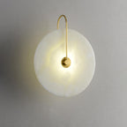 Three-quarter view of the gold Elaris wall light lit, showing the gentle dish shape of the disc.