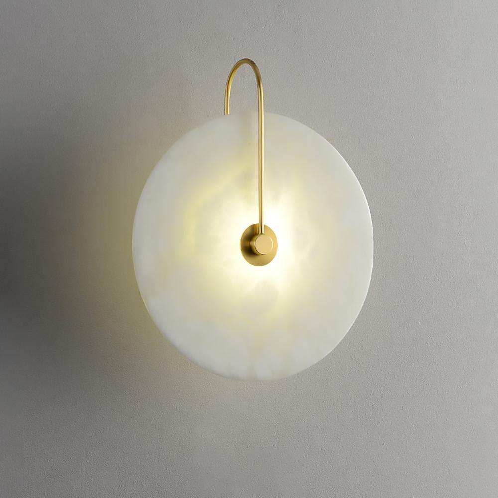 Three-quarter view of the gold Elaris wall light lit, showing the gentle dish shape of the disc.