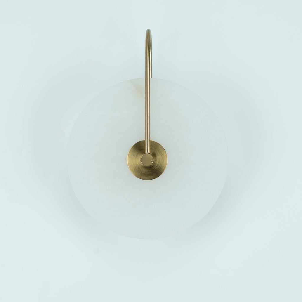 Unlit Elaris wall light in antique brass, close view of the arched arm and round centre mount.