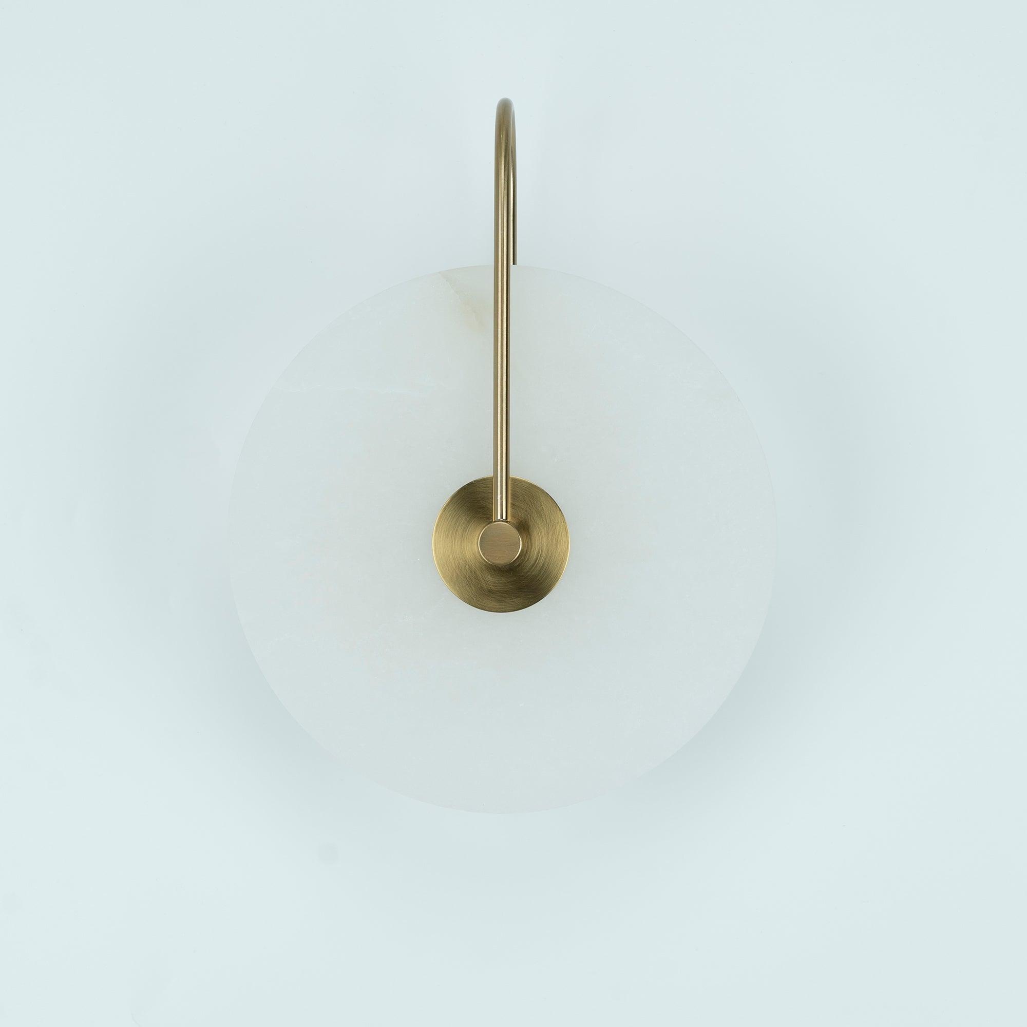 Unlit Elaris wall light in antique brass, close view of the arched arm and round centre mount.