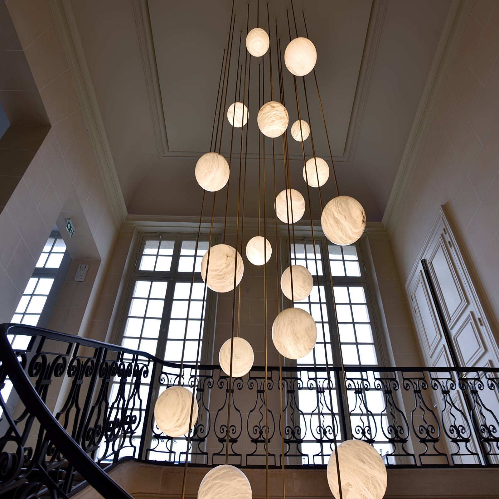 Looking up at the cluster in a classical stairwell with tall windows and an iron balustrade.