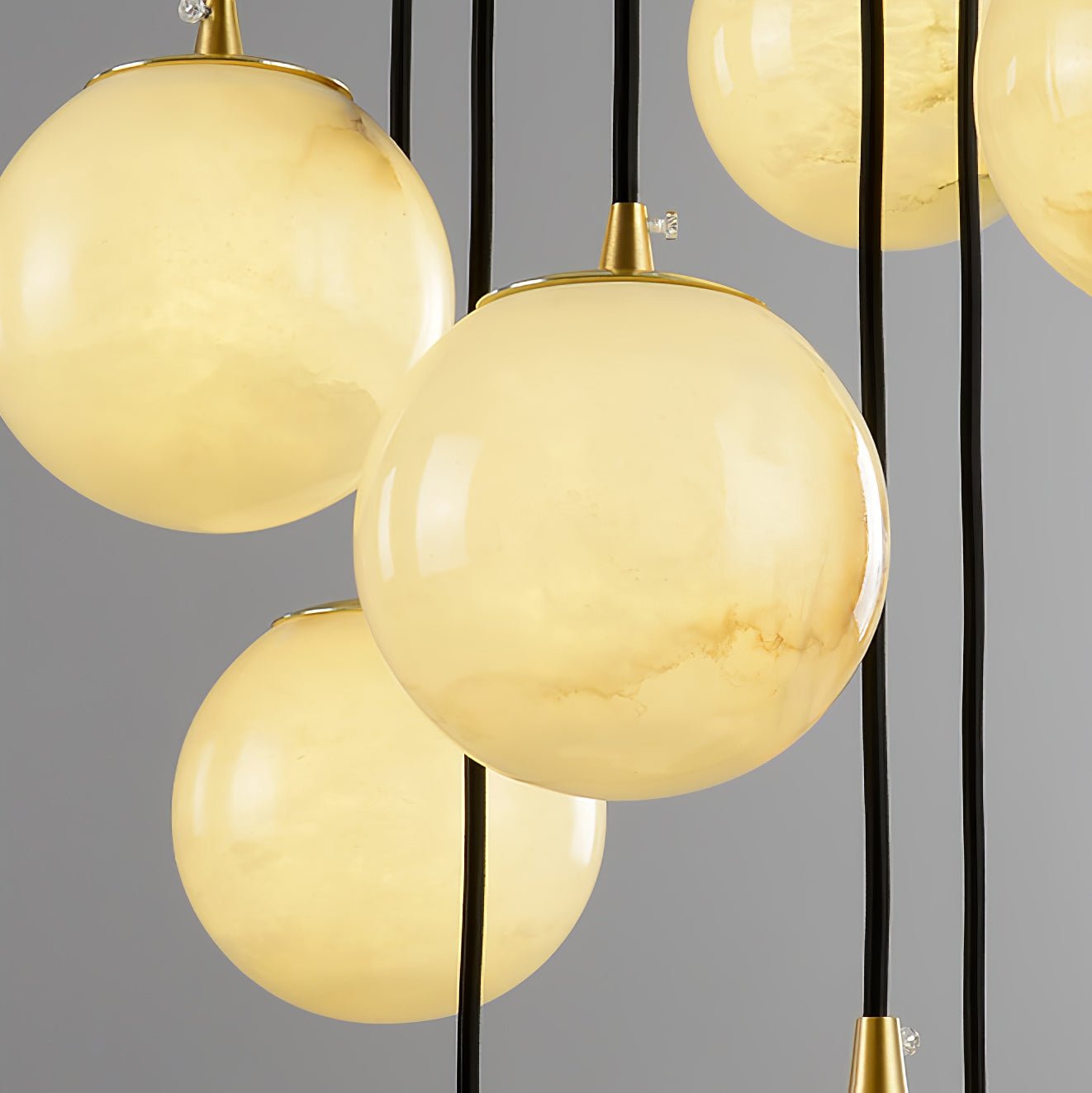 Close crop of several alabaster balls overlapping, brass fittings and black cords behind.