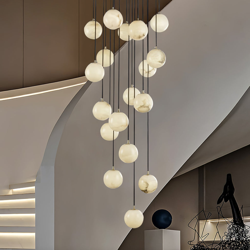 The chandelier lit in a curved modern stairwell, alabaster veining visible in each ball.