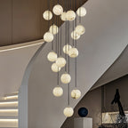 The chandelier lit in a curved modern stairwell, alabaster veining visible in each ball.