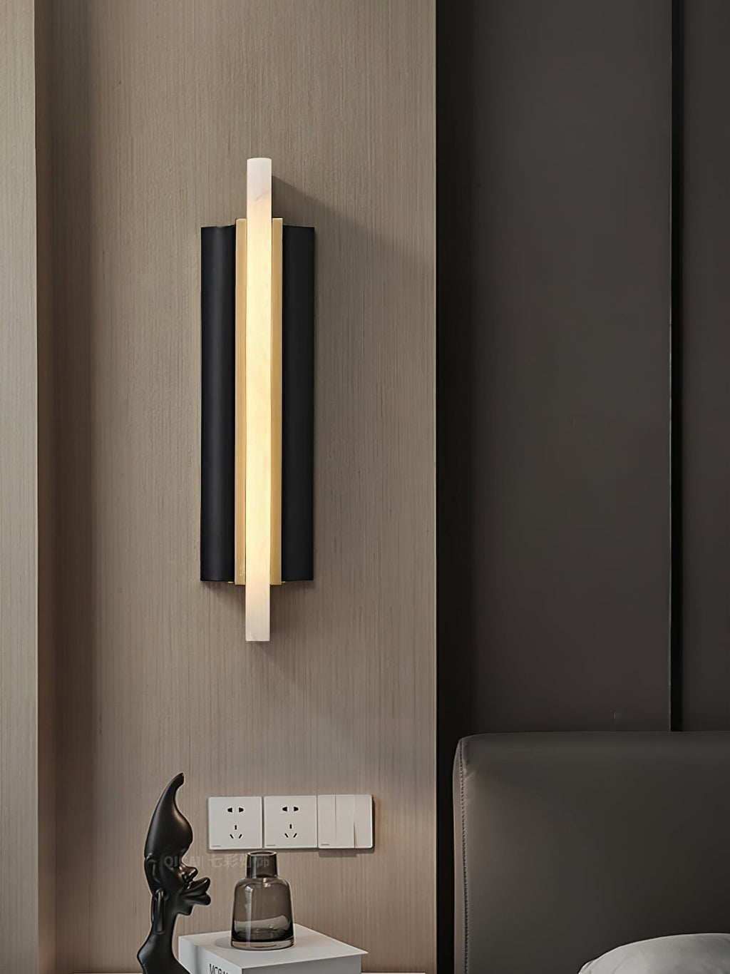 The fixture lit on wood panelling beside a bed, sockets and a glass vase on the table below.