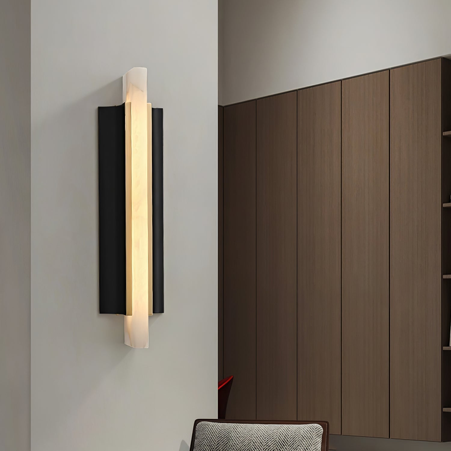 Wider room view of the Aurelian alabaster sconce lit on a white corner wall opposite wood cabinetry