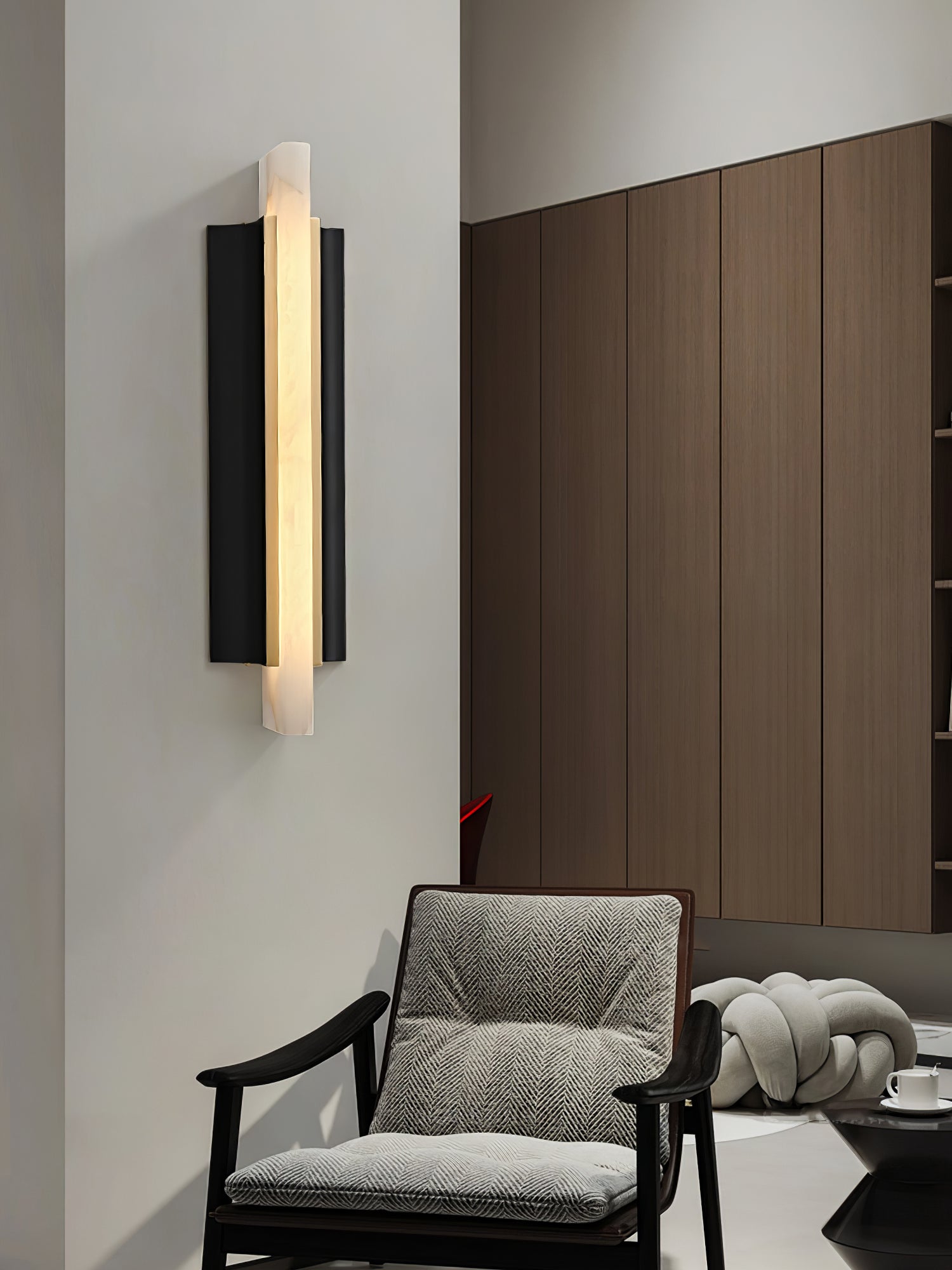 Lit on a white wall beside walnut cabinets, a grey armchair and knot cushion below.