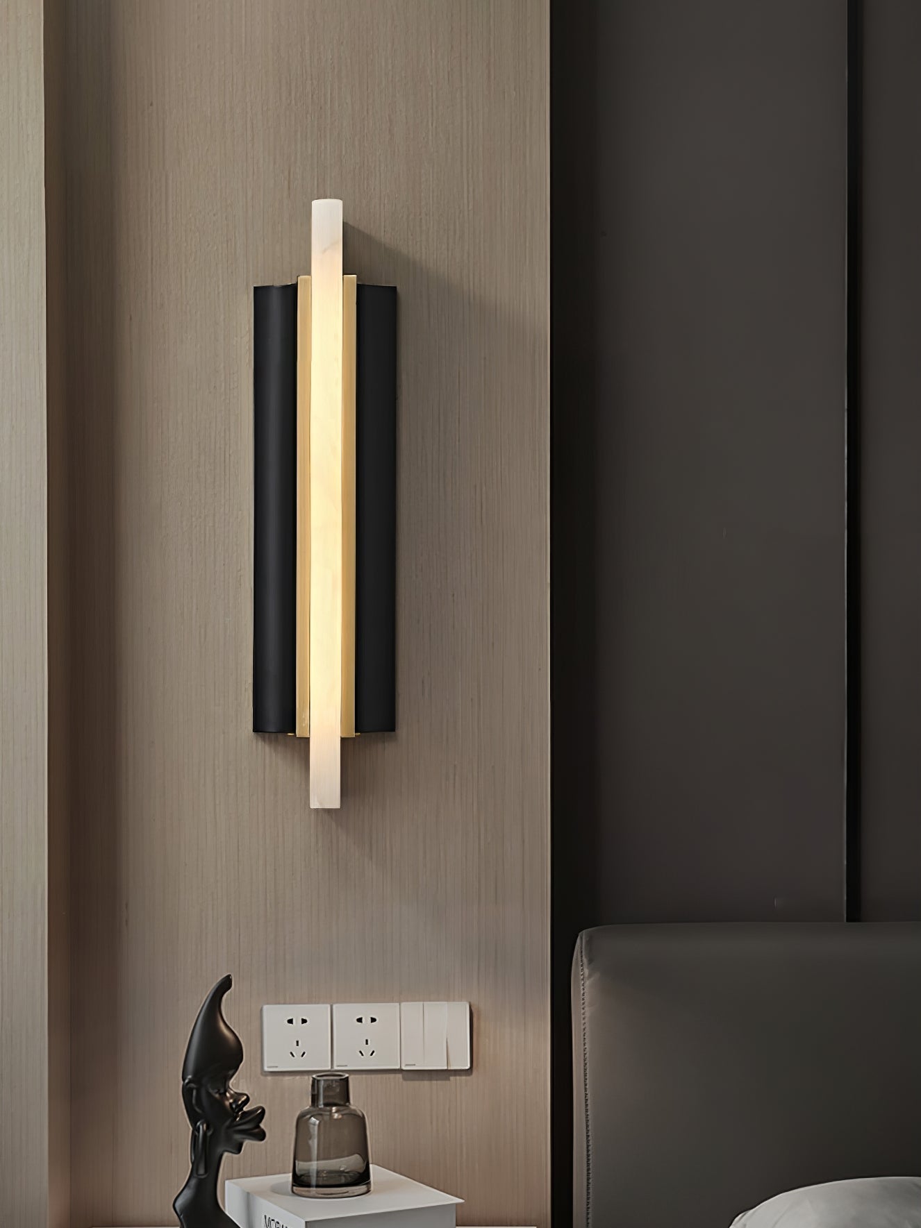 Lit on a wood-panelled wall above a bedside table with a black figurine and glass vase.