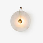 Kristy wall lamp photographed on white, the arched brass arm hooking over the top of the lit disc.