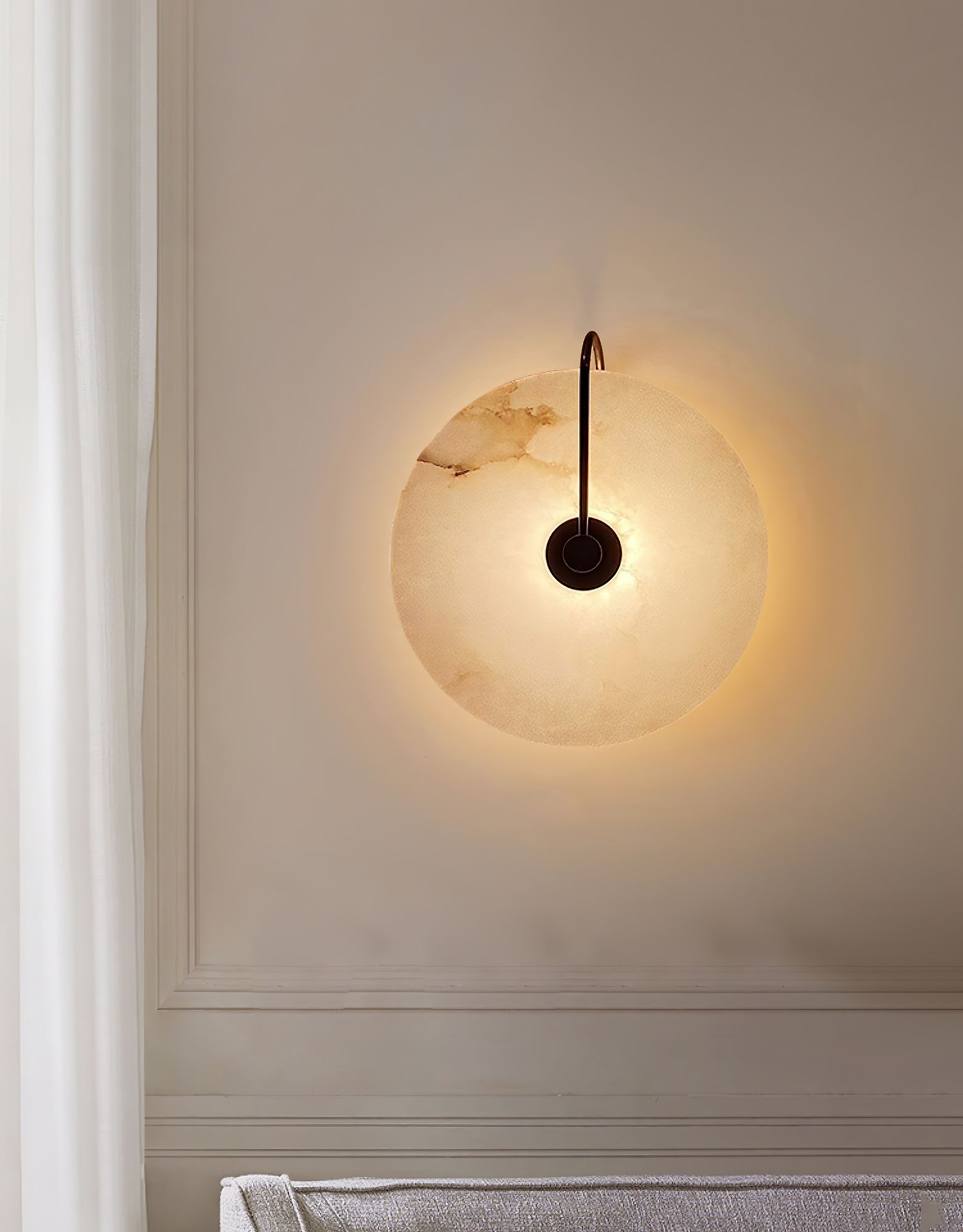 Black Elaris wall light lit on a panelled cream wall beside a curtain, its glow ringing the disc.