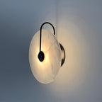 Side view of the lit black Elaris wall light, showing the disc's shallow profile and wall fitting.