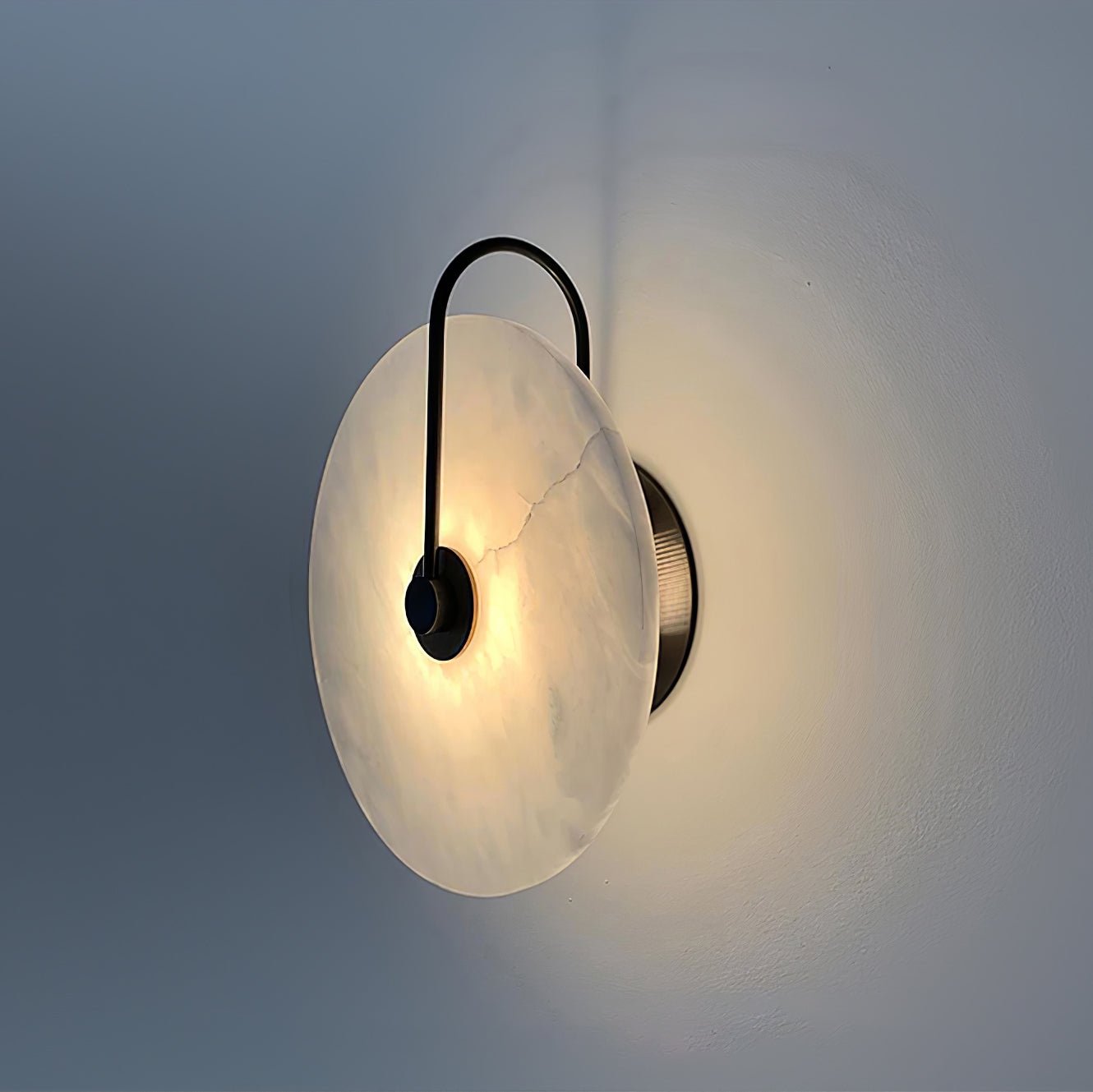 Side view of the lit black Elaris wall light, showing the disc's shallow profile and wall fitting.