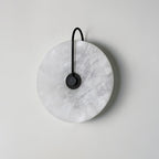 Kristy wall lamp unlit in the black-arm finish, grey marbled veining visible across the stone disc.
