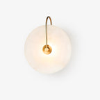 Studio shot of the Kristy wall lamp on a plain white background, brass arm arching over the lit disc.