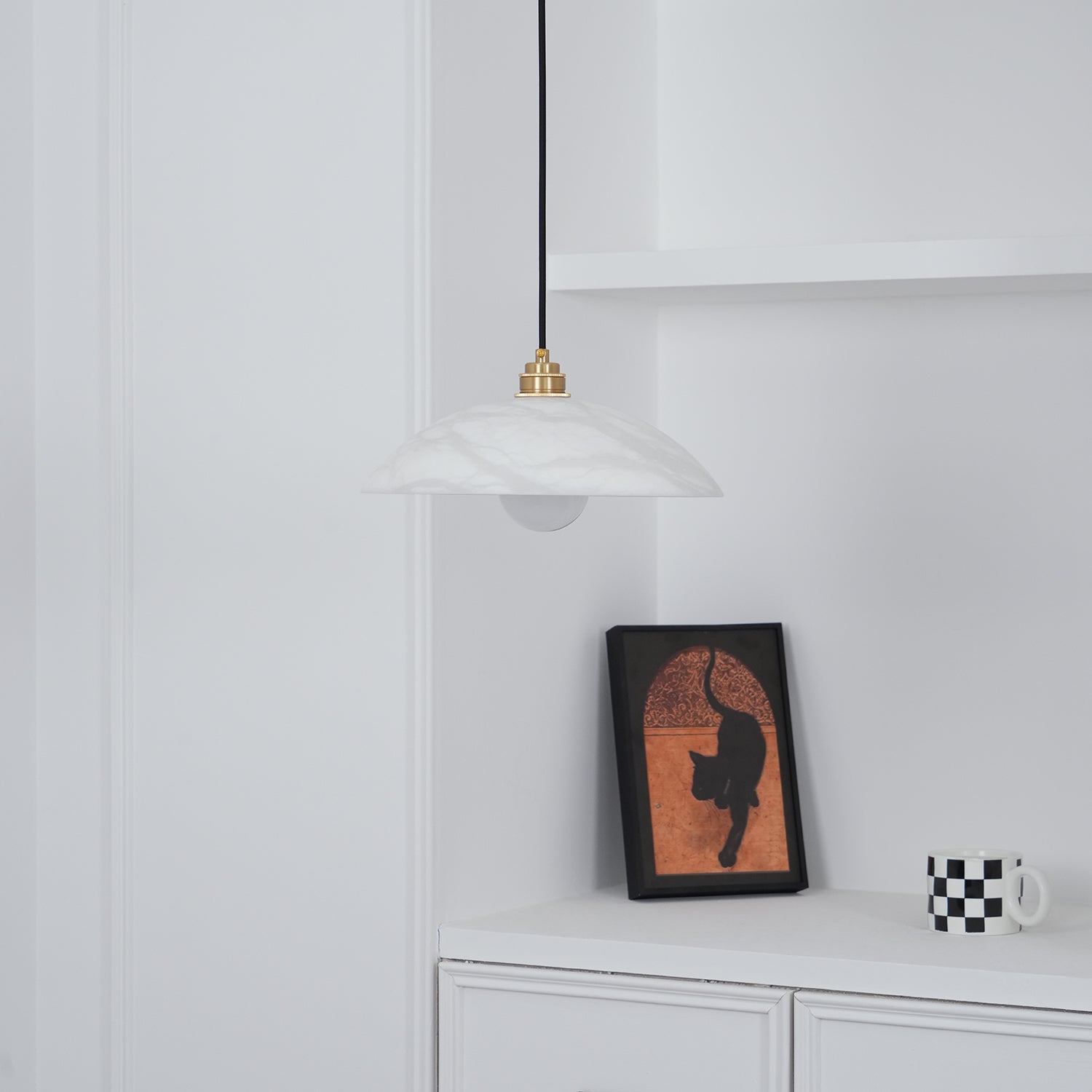 Unlit Nerea pendant in a white panelled alcove beside a framed cat print and checkerboard mug.
