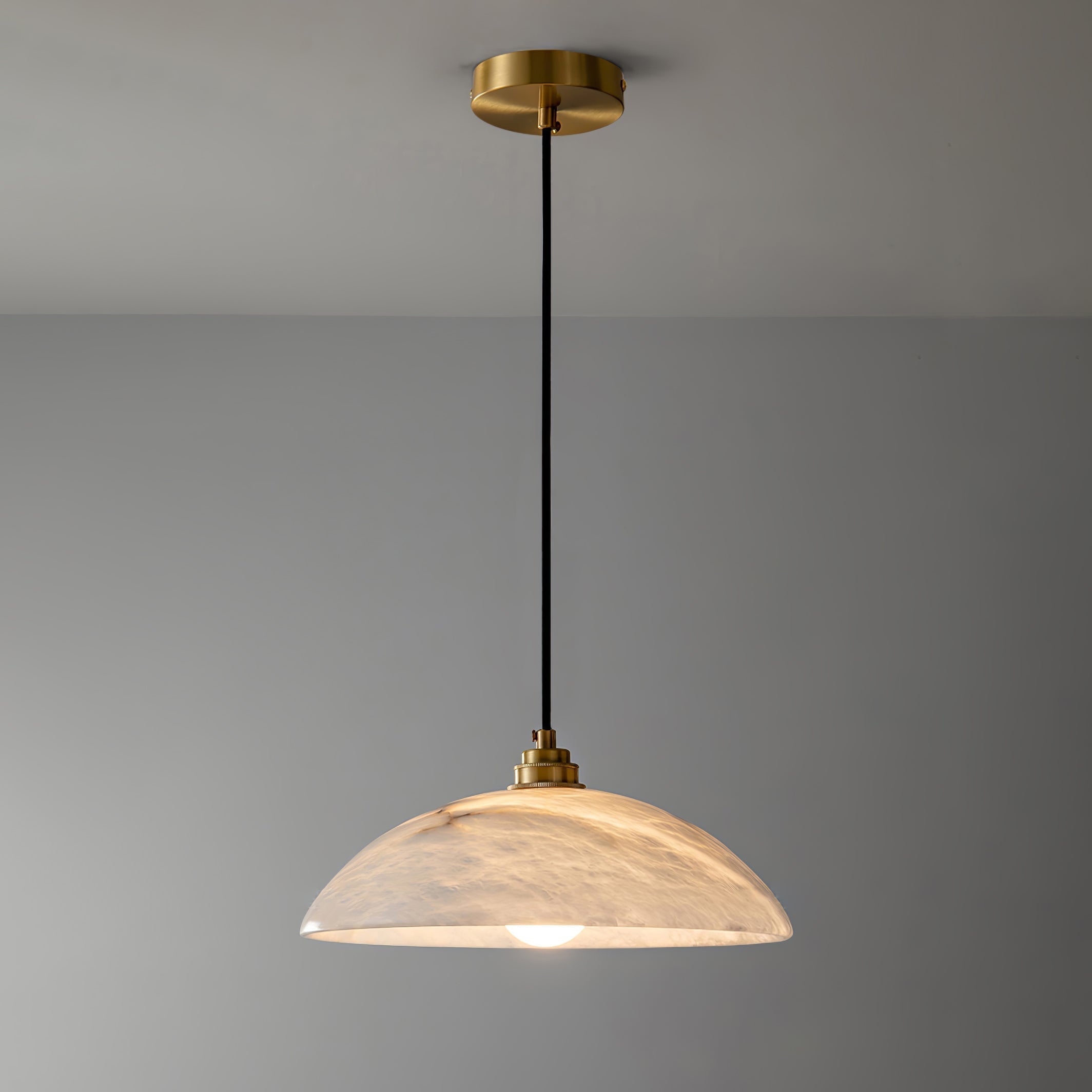 Nerea pendant lit and shown full length, brass canopy at the ceiling above a long black cord.