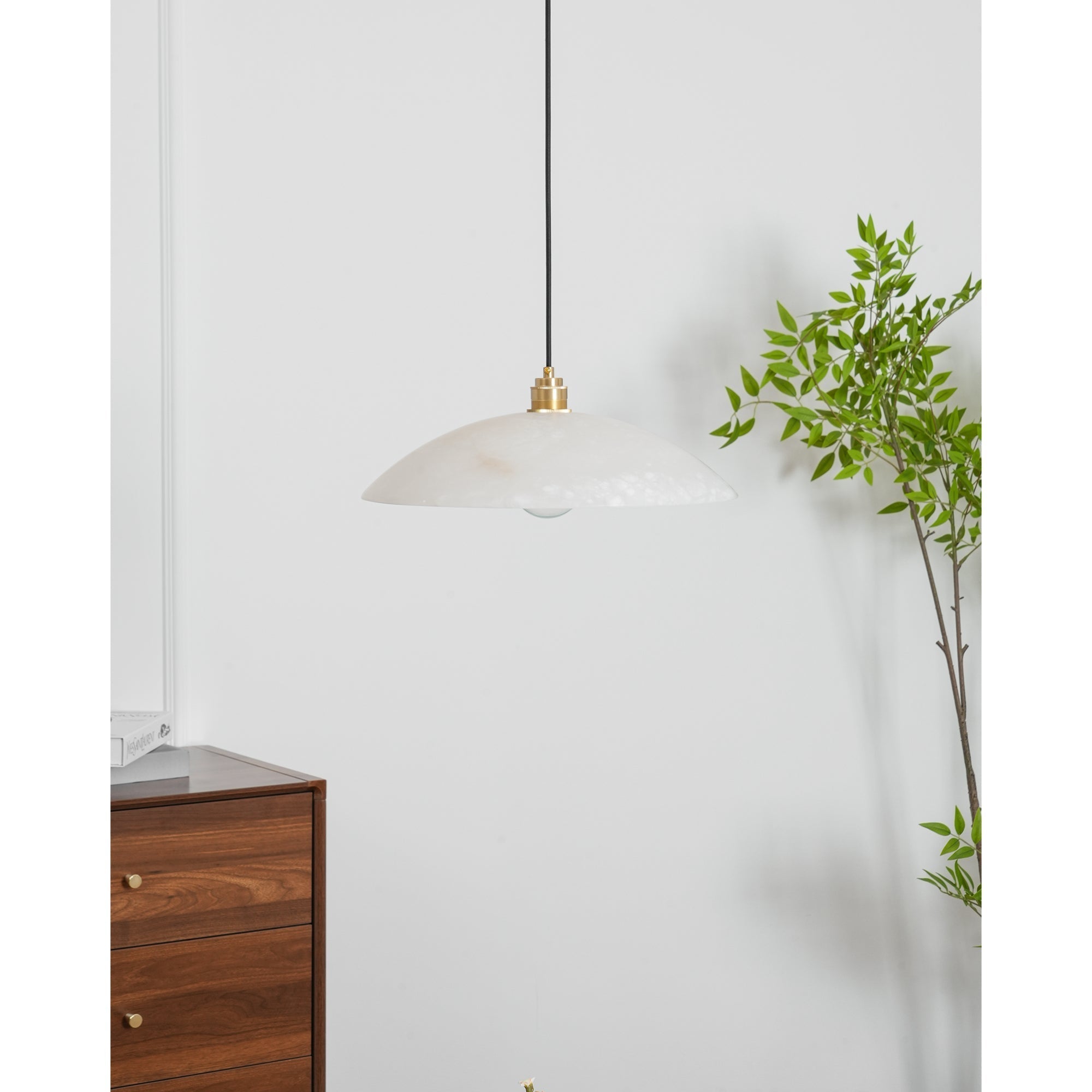 Nerea pendant unlit beside a leafy branch, with a walnut chest of drawers to the left.