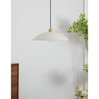 Unlit Nerea pendant casting a soft daylight shadow on the wall, a plant framing the right.