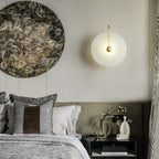 Closer crop of the gold Elaris wall light glowing on a bedroom wall next to a round wall artwork.