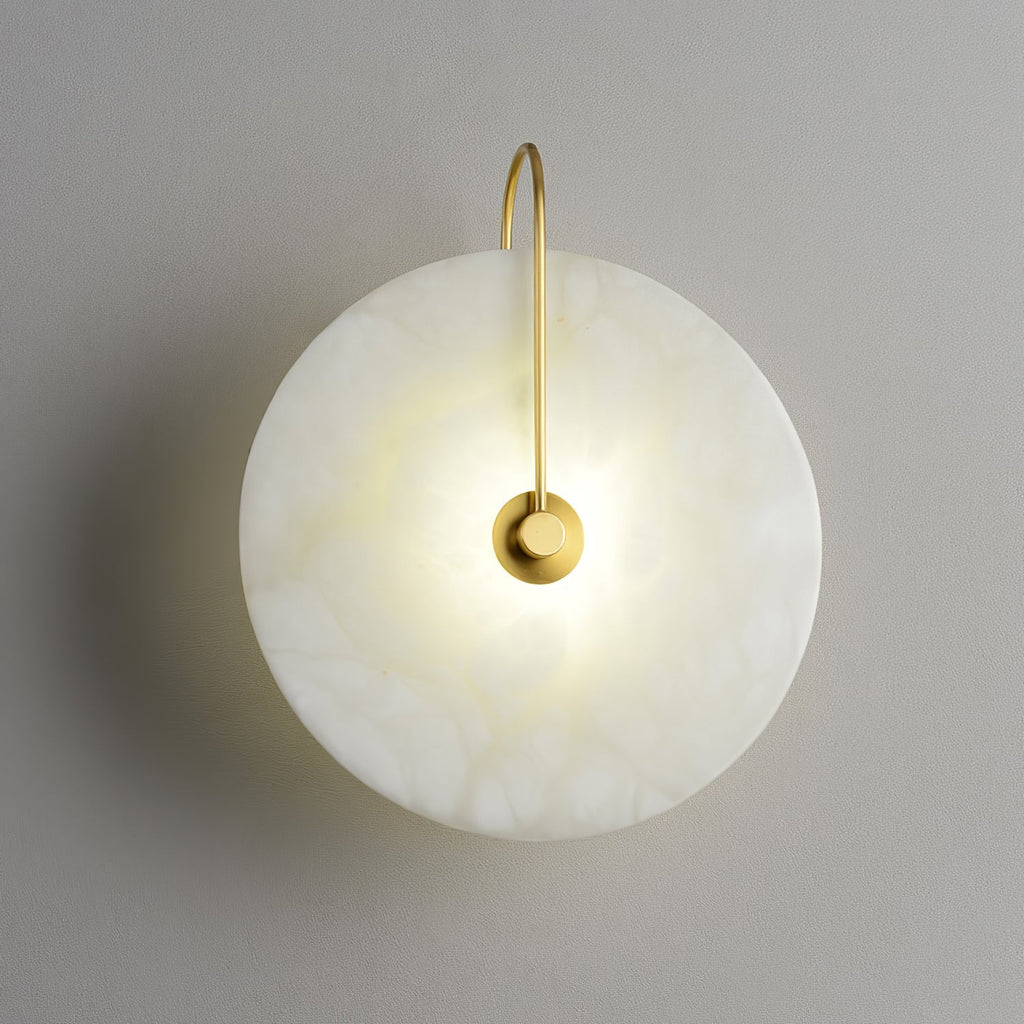 Lit gold Elaris wall light on a grey wall, the arm arching from the top edge to the centre mount.