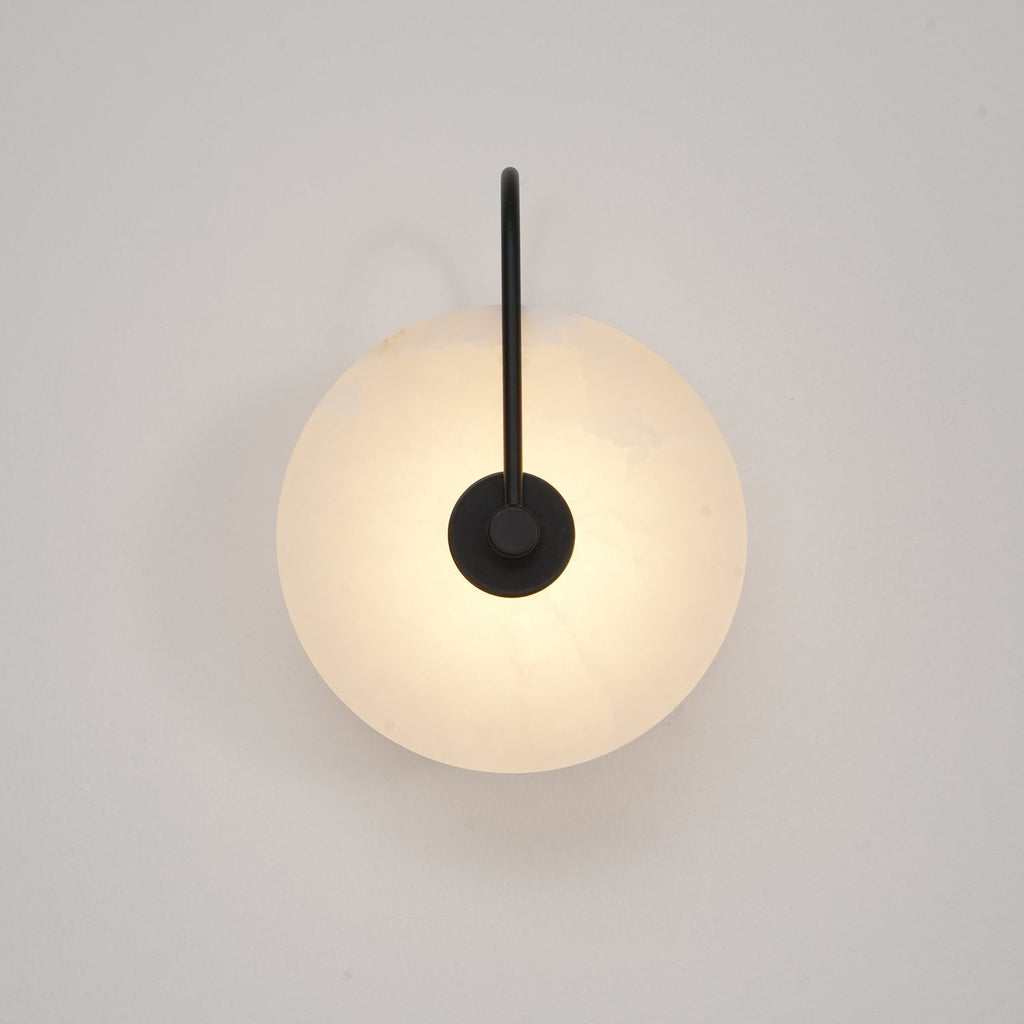 Softly lit black Elaris wall light on an off-white wall, the disc glowing from behind the mount.