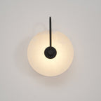 Softly lit black Elaris wall light on an off-white wall, the disc glowing from behind the mount.