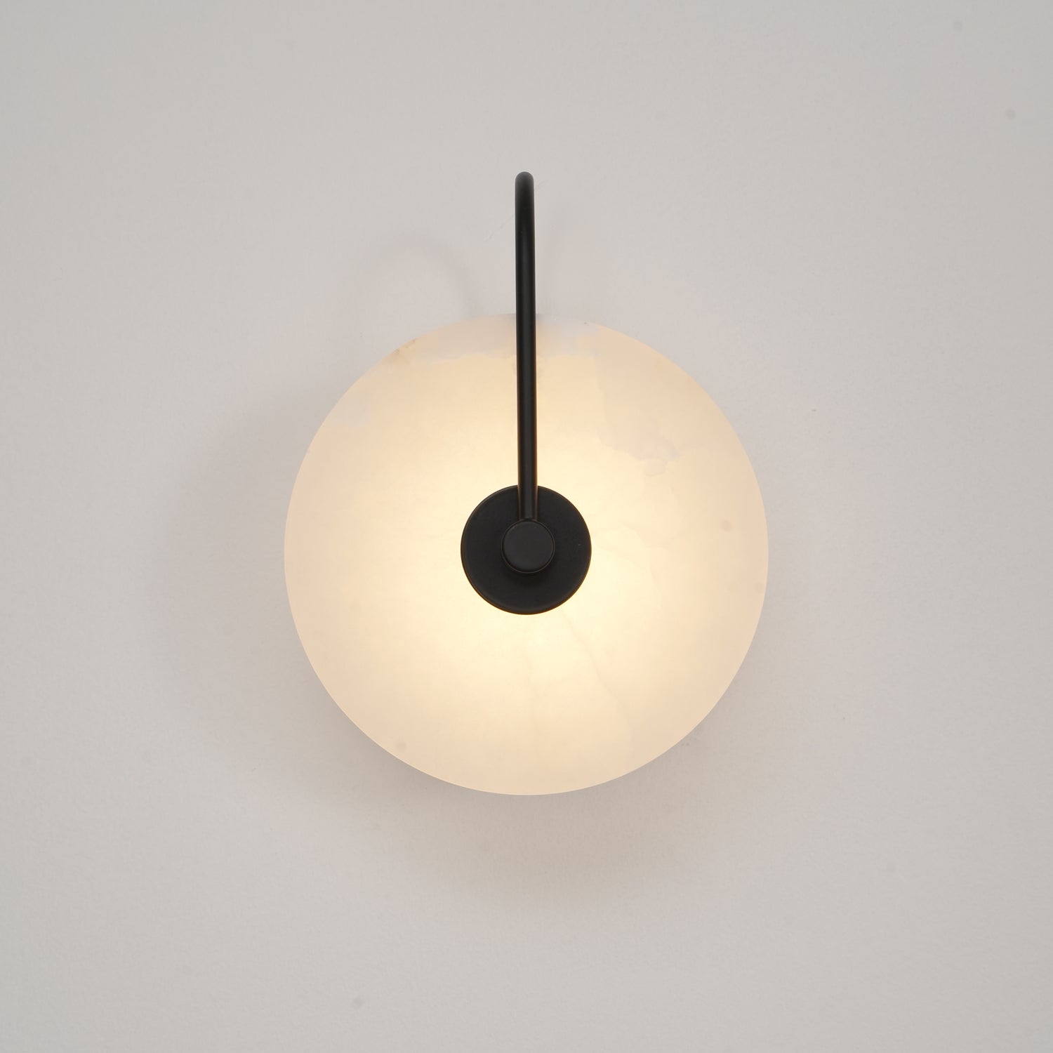 Softly lit black Elaris wall light on an off-white wall, the disc glowing from behind the mount.