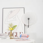 Unlit black Elaris wall light on a white wall in a styled corner with books, prints and flowers.