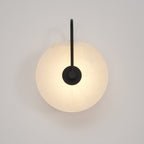 Black-arm Elaris wall light lit front-on, its warm glow spreading evenly across the alabaster disc.