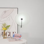 Wider view of the black Elaris wall light unlit on a white wall next to a framed print and vase.