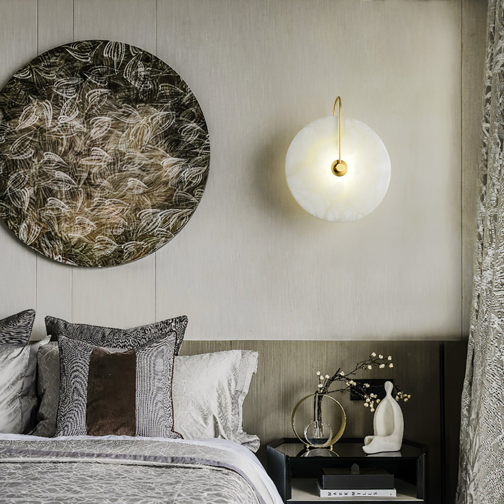 Gold Elaris wall light lit beside a large round artwork above a layered, cushion-piled bed.