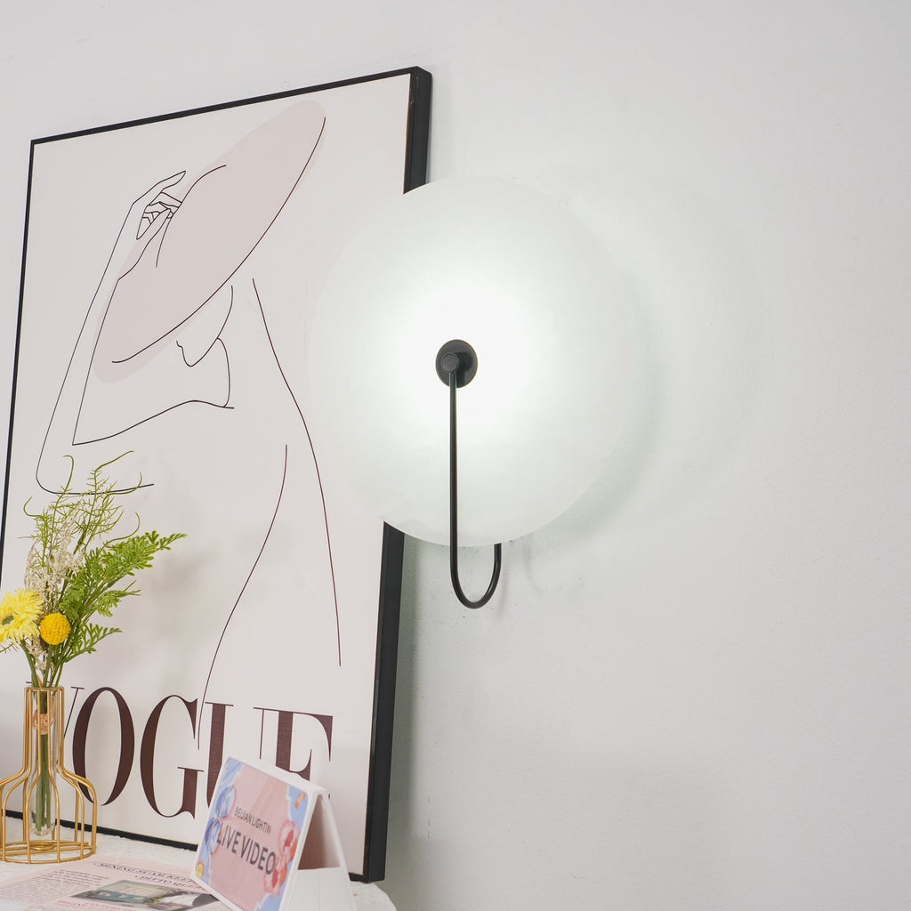 Angled view of the unlit black Elaris wall light catching daylight beside a framed print.