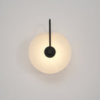 Black Elaris wall light lit low and soft, the disc face evenly bright against an off-white wall.