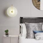 Wider bedroom view of the gold Elaris wall light lit beside a rattan headboard and bedside cabinet.