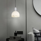 Clérachic alabaster pendant light glowing in a taupe-walled room, hanging near a round mirror and a perfume bottle on a box.