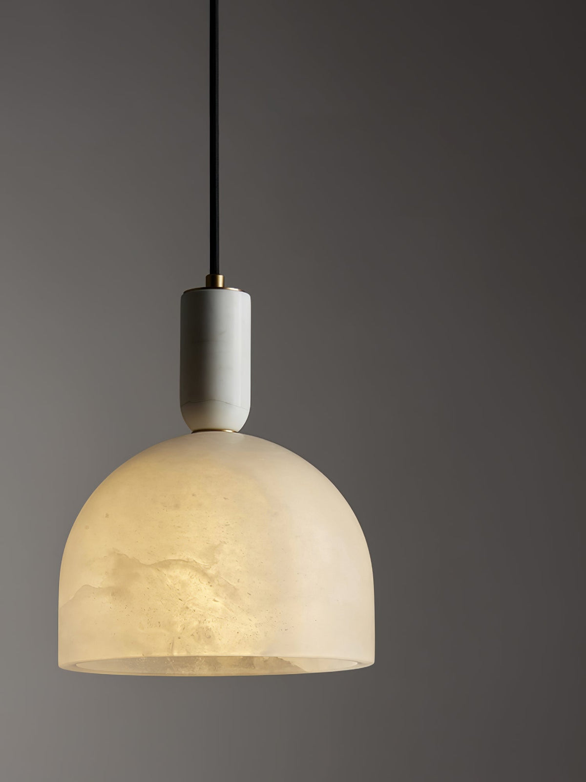 Clérachic alabaster pendant light against a dark charcoal wall, its warm glow standing out sharply in the low light.