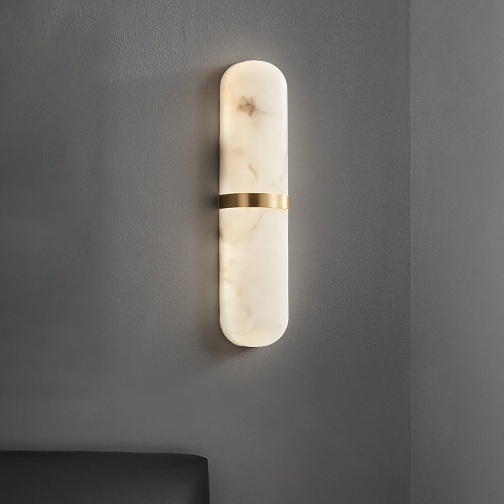 Clérachic slim alabaster wall lamp with brass band, lit, casting a soft halo on a charcoal grey wall