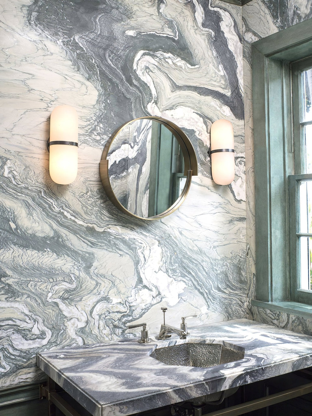 A Clérachic pair of black-banded alabaster wall lamps flanking a round mirror above a marble washbasin