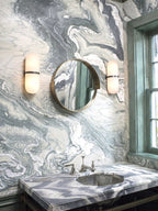 A Clérachic pair of black-banded alabaster wall lamps flanking a round mirror above a marble washbasin