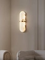 Clérachic alabaster wall lamp lit in a beige panelled corner above a cream sofa, warm glow on the wall