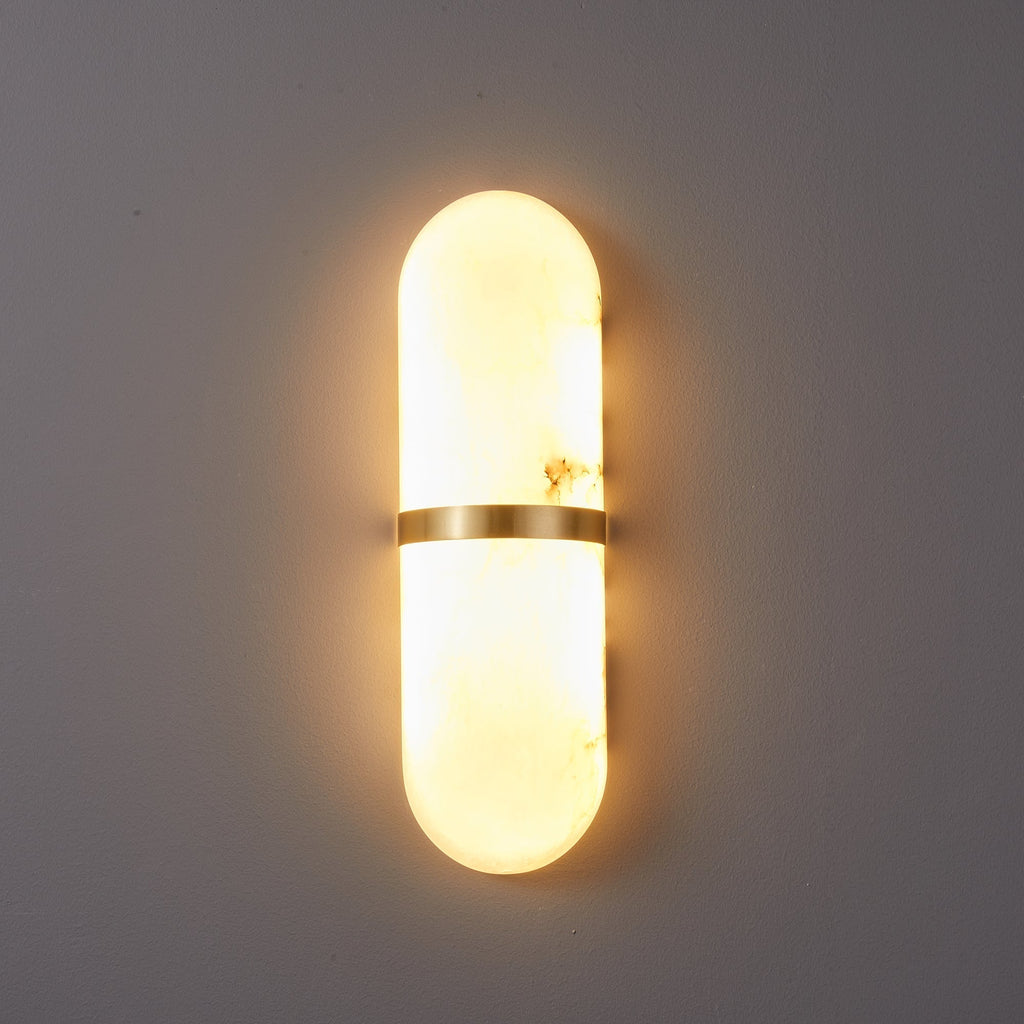 The Clérachic alabaster wall lamp lit head-on, brass band splitting the glow into upward and downward halves